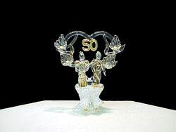 50th anniversary wedding cake top with a solid glass bride figurine, solid glass group figurine, solid glass heart flower and leaves wrapped around a solid glass heart.
